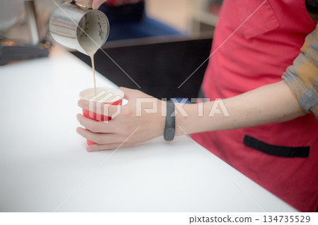 Barista in a red apron pours coffee in a plastic cup. Close up shot Barista in a red apron pours coffee in a plastic cup. Close up shot 134735529