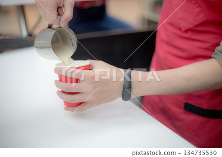 Barista in a red apron pours coffee in a plastic cup Barista in a red apron pours coffee in a plastic cup 134735530