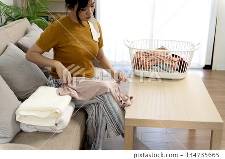 A young woman is sitting in the living room folding clothes modern woman A young woman is sitting in the living room folding clothes modern woman 134735665