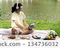 Young woman sits comfortably on a mat on a grassy lawn in a park 134736032