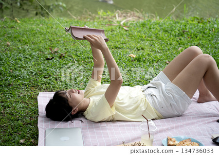 Young woman is lying down reading a book and relaxing on a mat 134736033