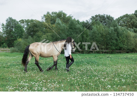 Woman walking with horse in green meadow, rear view, peaceful rural lifestyle and connection with animals in nature. Young woman with horse in countryside meadow, showing equestrian bond, trust Woman walking with horse in green meadow, rear view, peaceful rural lifestyle and connection with animals in nature. Young woman with horse in countryside meadow, showing equestrian bond, trust 134737450