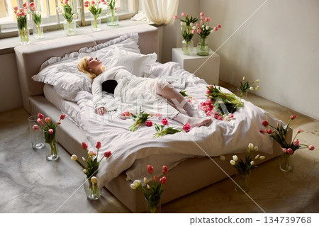 Woman resting on floral bed, Serene woman naps on bohemian bed adorned with tulips and petals Woman resting on floral bed, Serene woman naps on bohemian bed adorned with tulips and petals 134739768