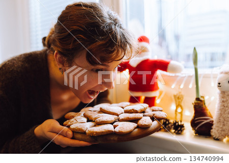 young woman holding gingerbread cookies on a wooden round board 134740994