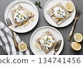 Different plates with flatbread topped with yogurt, corn, and herbs on a gray table 134741456