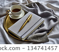 Coffee cup and notebook on a tray with fabric on a table in a soft light setting 134741457