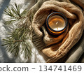 Candle resting on knitted sweater with pine branches in cozy indoor setting 134741469