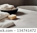 Soft towels and soap placed on a light surface near a bathtub in a bathroom setting 134741472