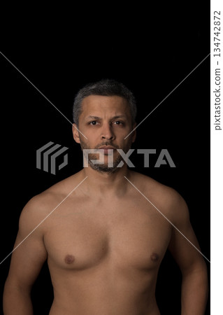 A man with a shaved chest stands in front of a black background A man with a shaved chest stands in front of a black background 134742872