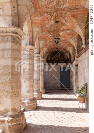 A long hallway with pillars and a plant in a vase A long hallway with pillars and a plant in a vase 134742895