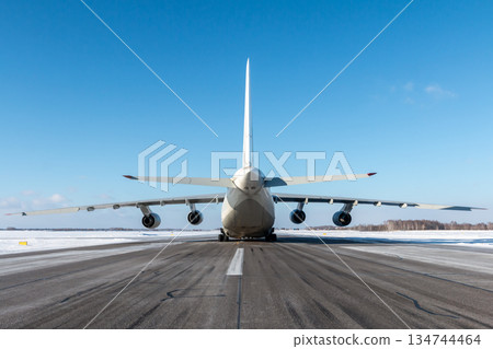 Large heavy transport aircraft on the runway of winter airport. Rear view Large heavy transport aircraft on the runway of winter airport. Rear view 134744464