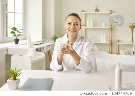 Young smiling woman cosmetologist sitting in beauty spa salon and looking at camera. 134744769