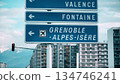Road signs pointing to Grenoble Alpes Isere airport with alpine mountains and urban buildings 134746241