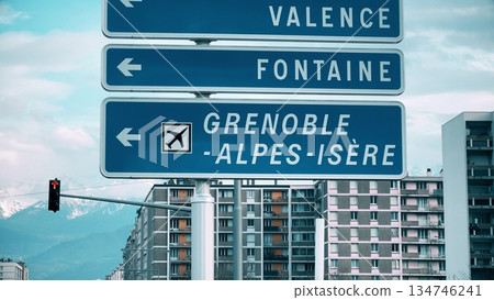 Road signs pointing to Grenoble Alpes Isere airport with alpine mountains and urban buildings 134746241