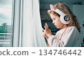Young child using smartphone while wearing headphones at home near window 134746442