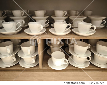 Rows of white porcelain cups and saucers on wooden shelves Rows of white porcelain cups and saucers on wooden shelves 134746724