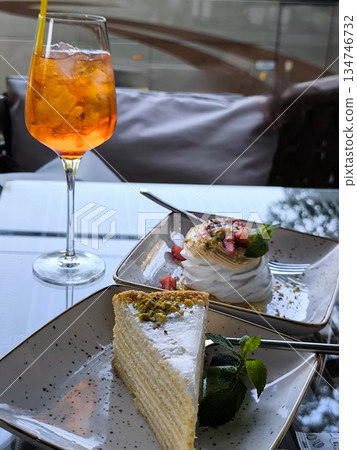 Summer fun: an orange cocktail and two exquisite desserts on a glass table 134746732