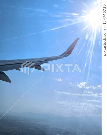 Airplane wing, bright sun and mountains, view from the window Airplane wing, bright sun and mountains, view from the window 134746739