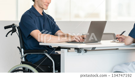 辦公室裡，一名坐在輪椅上的男性員工正在辦公桌前工作。 134747192