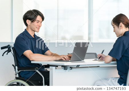 辦公室裡，一名坐在輪椅上的男性員工正在辦公桌前工作。 134747193