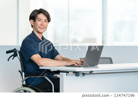 辦公室裡，一名坐在輪椅上的男性員工正在辦公桌前工作。 134747196