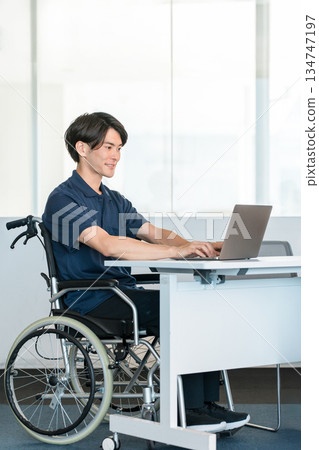A male staff member in a wheelchair working at a desk in the office A male staff member in a wheelchair working at a desk in the office 134747197