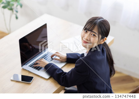 Young businesswoman smiling at the camera while working on a computer Young businesswoman smiling at the camera while working on a computer 134747448