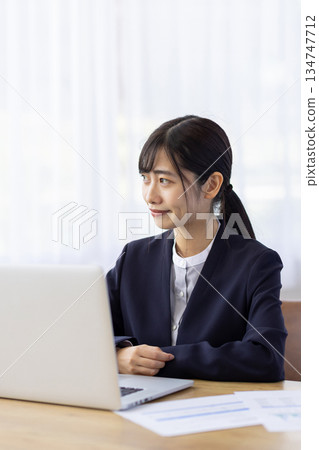 A young woman in a suit looking out the window between computer work 134747712