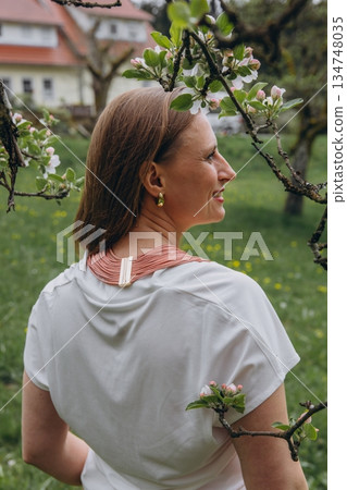 Happy middle-aged woman enjoying nature and embracing herself in spring field. Concept of self-love, female health, emotional balance, mindfulness, and positive aging 134748035