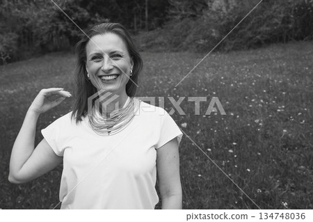 Happy middle-aged woman enjoying nature and embracing herself in spring field. Concept of self-love, female health, emotional balance, mindfulness, and positive aging Happy middle-aged woman enjoying nature and embracing herself in spring field. Concept of self-love, female health, emotional balance, mindfulness, and positive aging 134748036