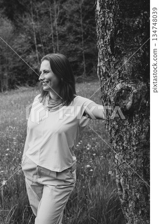 Smiling middle-aged woman standing near blooming tree in spring garden. Concept of female health, hormonal balance, wellness, and natural beauty in midlife Smiling middle-aged woman standing near blooming tree in spring garden. Concept of female health, hormonal balance, wellness, and natural beauty in midlife 134748039