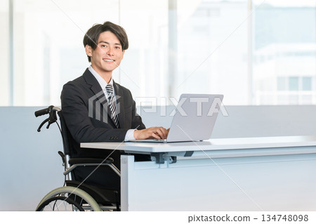 A businessman in a suit in a wheelchair working at his desk in the office 134748098