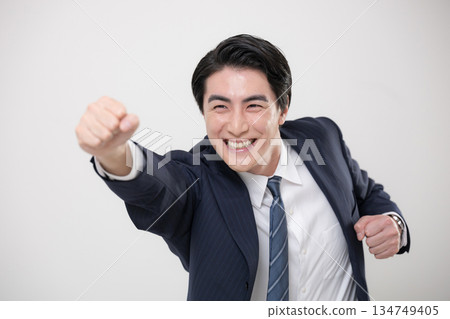 A jumping and dynamic businessman in a suit posing with a fist pump to grasp his goal or future A jumping and dynamic businessman in a suit posing with a fist pump to grasp his goal or future 134749405