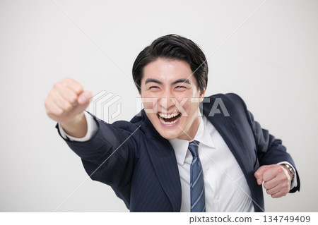 一位身穿西裝、活力四射的商人，揮舞著拳頭，擺出姿勢，彷彿在擁抱他的目標或未來。 134749409