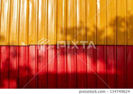 Vibrant metal wall with red and yellow panels and tree shadow creating dynamic texture for modern architectural backgrounds 134749624