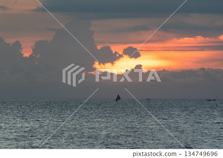 Serene sunset over the ocean with sailing boat silhouette and dramatic clouds formation creating peaceful seascape with natural light and copy space 134749696