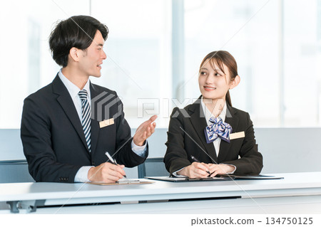 Businessmen and businesswomen in suits standing at a desk (interviewer, company information session) Businessmen and businesswomen in suits standing at a desk (interviewer, company information session) 134750125