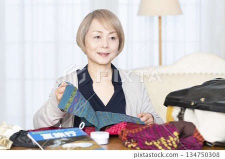Senior woman packing for a trip in the living room Senior woman packing for a trip in the living room 134750308