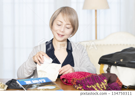 Senior woman packing for a trip in the living room Senior woman packing for a trip in the living room 134750311