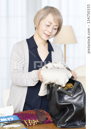 Senior woman packing for a trip in the living room Senior woman packing for a trip in the living room 134750335