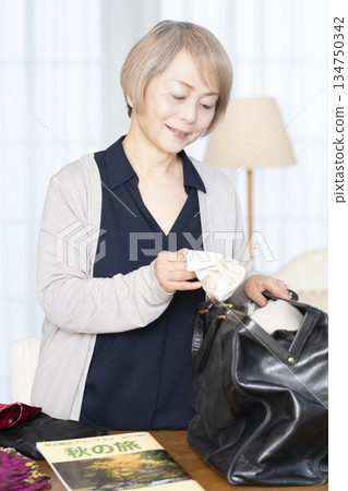 Senior woman packing for a trip in the living room 134750342