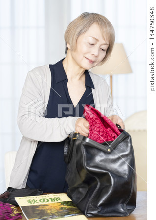 Senior woman packing for a trip in the living room Senior woman packing for a trip in the living room 134750348