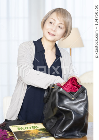 老婦人在客廳收拾行李準備旅行 老婦人在客廳收拾行李準備旅行 134750350