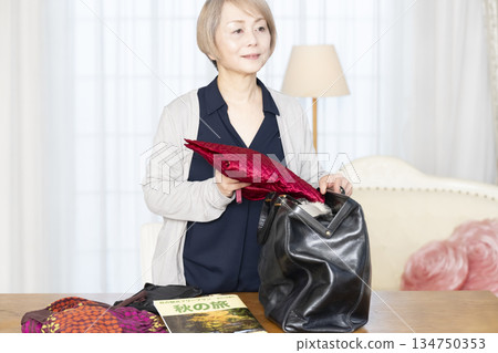 Senior woman packing for a trip in the living room Senior woman packing for a trip in the living room 134750353