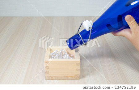 一隻藍色的酒瓶和一隻人手將清酒倒入枡中。 134752199