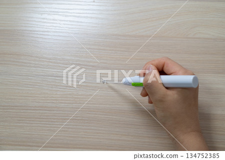 一手拿著一個發光的耳勺，背景是木紋。 134752385