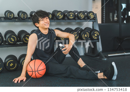 Young Asian man holding basketball and weight ball in gym 134753418