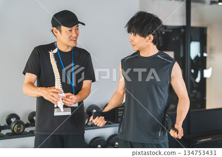 A trainer and a male gym member explaining using a skeletal specimen at a training gym A trainer and a male gym member explaining using a skeletal specimen at a training gym 134753431