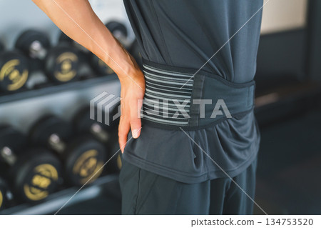 A man with back pain wearing a corset at the gym A man with back pain wearing a corset at the gym 134753520