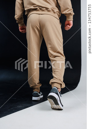 View of the back of an individual dressed in tan sweatpants and white sneakers View of the back of an individual dressed in tan sweatpants and white sneakers 134753755